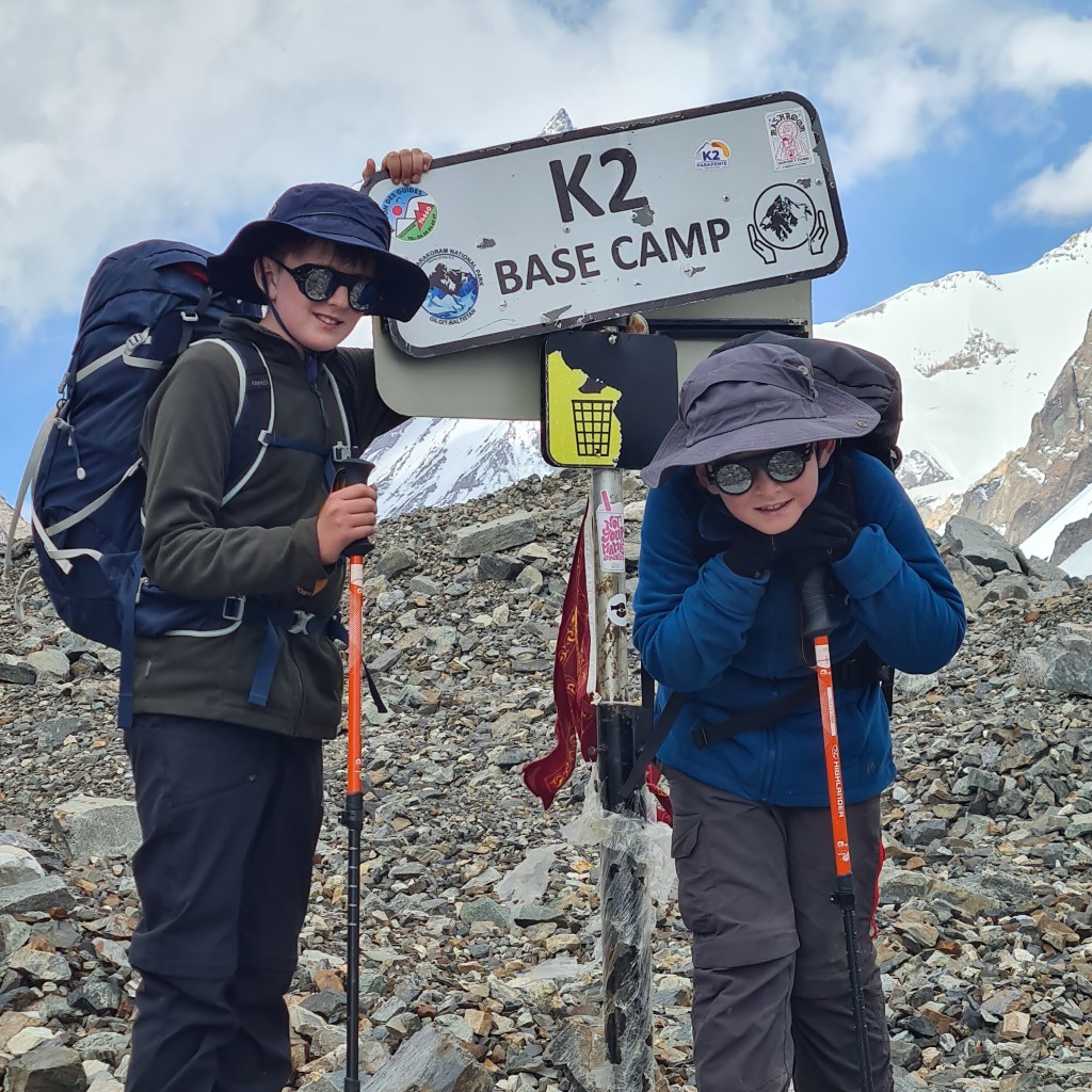 two biys standing at the sign of K2 Base camp