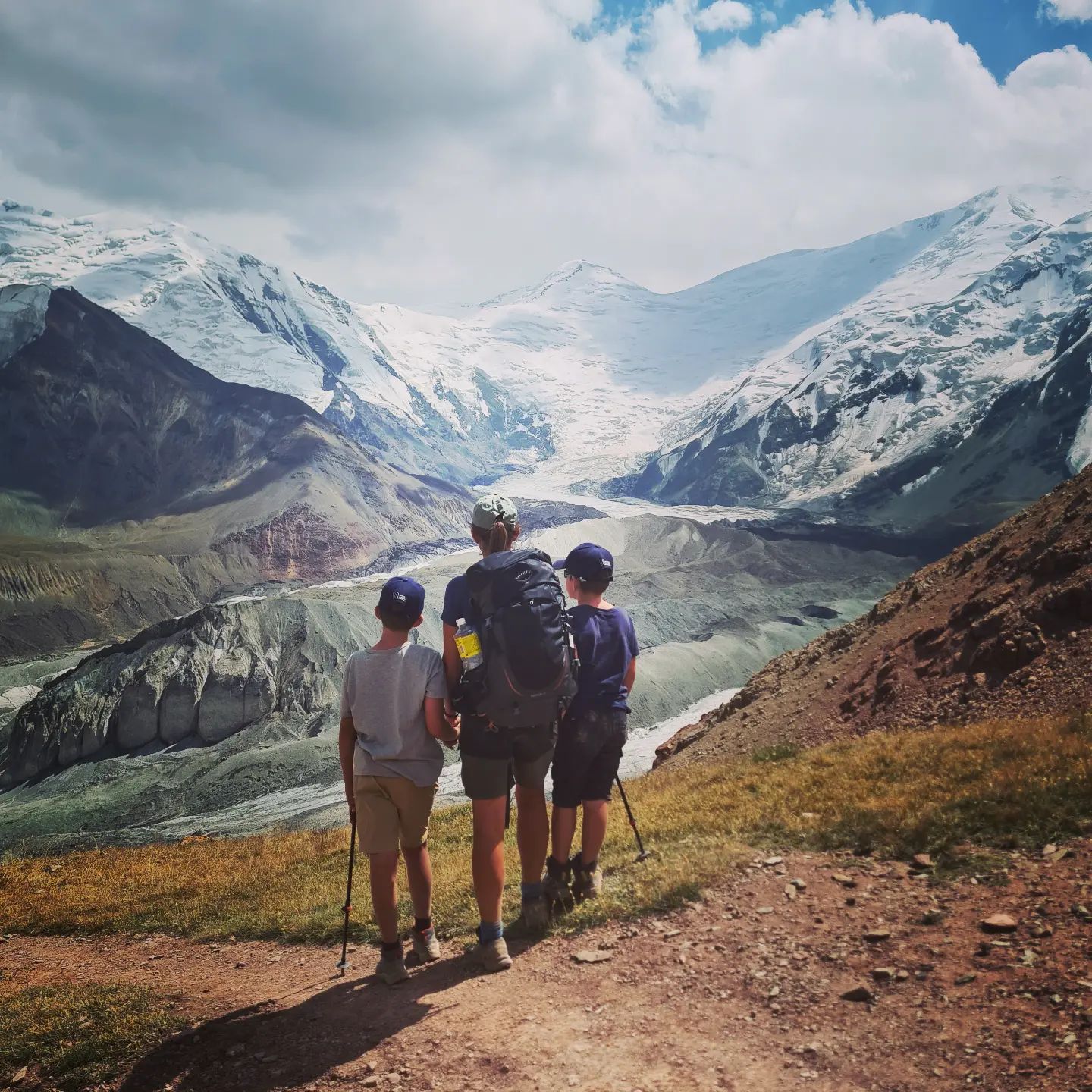 Mum and two suns standing in the mountains looking over a glacier. 