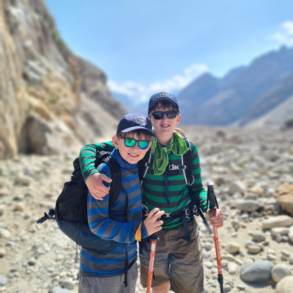 Two young boys hugging as they hike towards K2 in pakistan. Holding their Hiking poles. Allpart of our family adventure to Pakistan